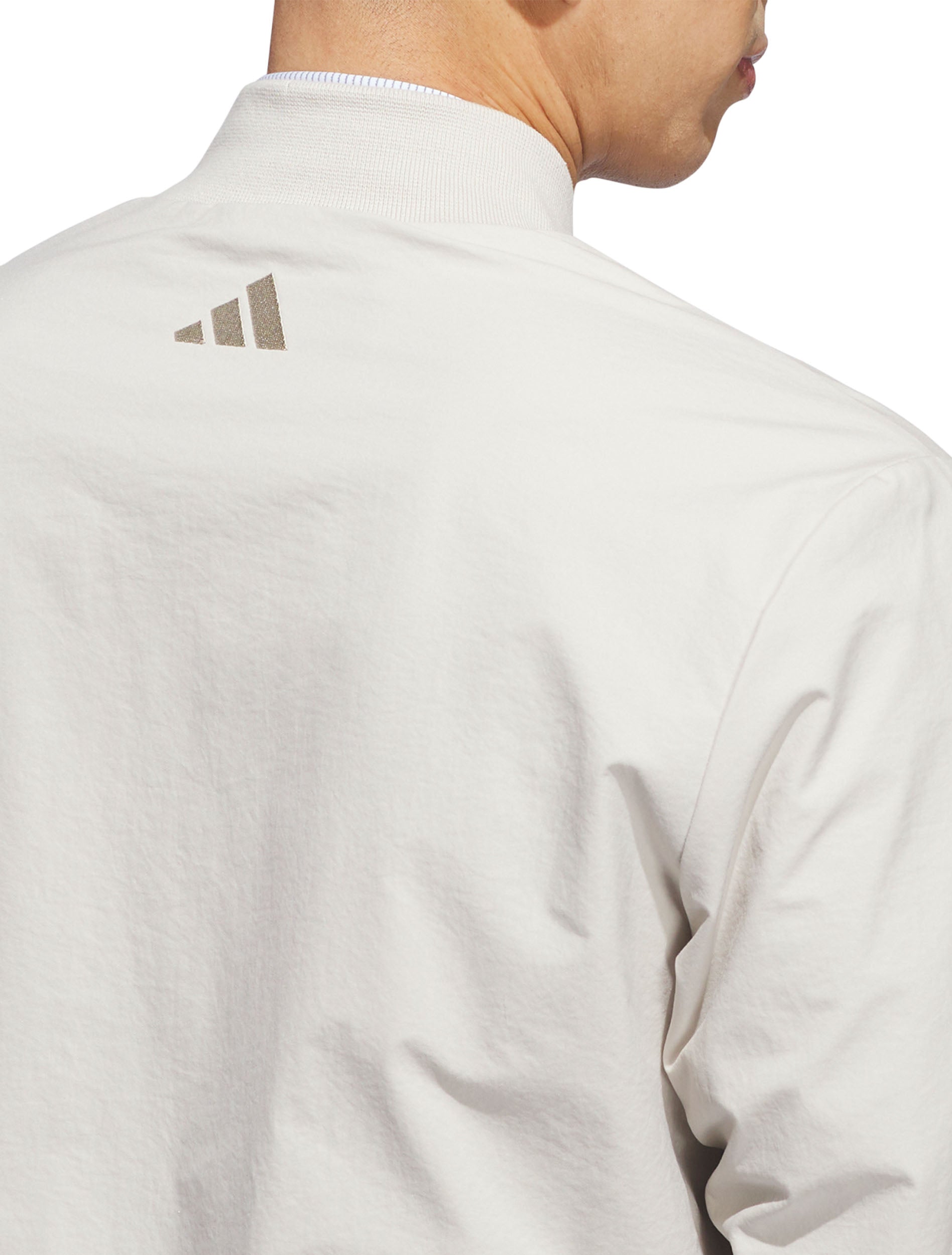 Close-up of the Adidas badge of sport below the collar on the back of the silver golf jacket