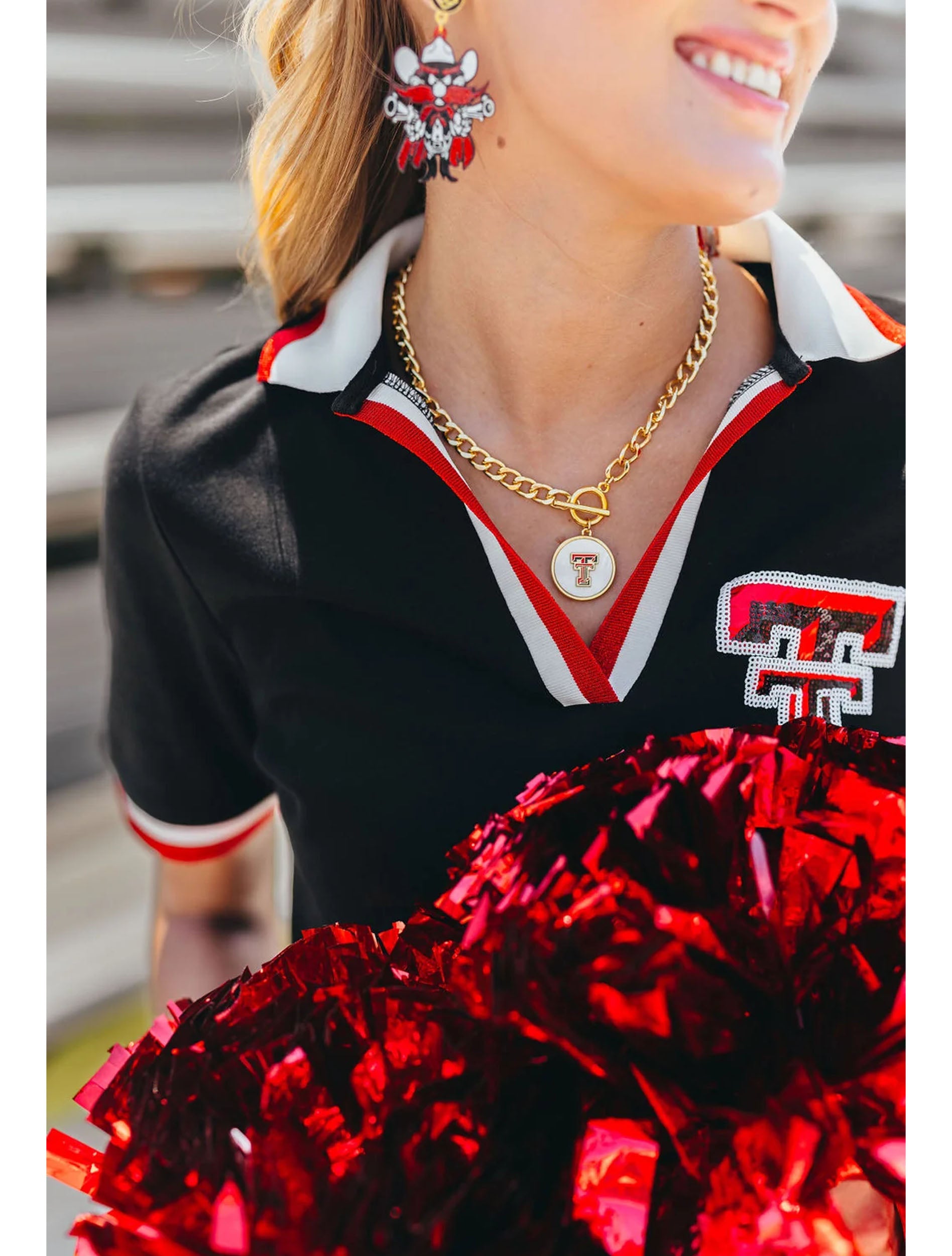 Model wearing the gold Texas Tech Double T toggle necklace with a black and red game day polo and pom poms