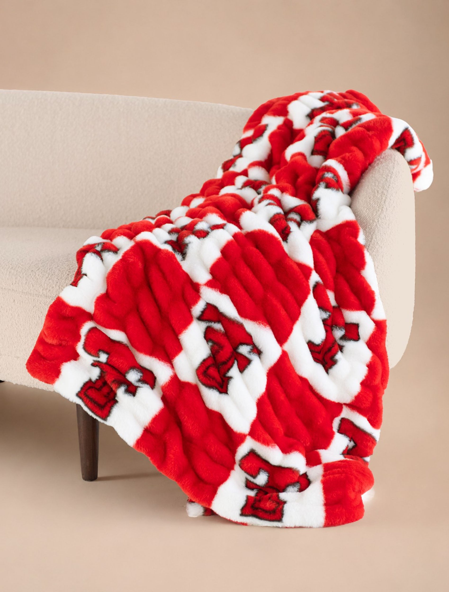 Red and white check Texas Tech plush blanket draped over a sofa, with a black Double T in each white square