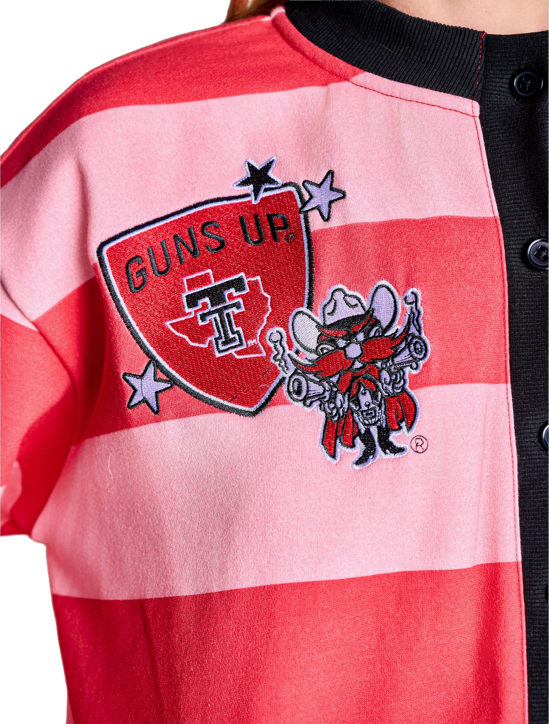 Close up of the front chest embroidery, a GUNS UP shield with the Texas outline and Double T beside Raider Red and lavender stars