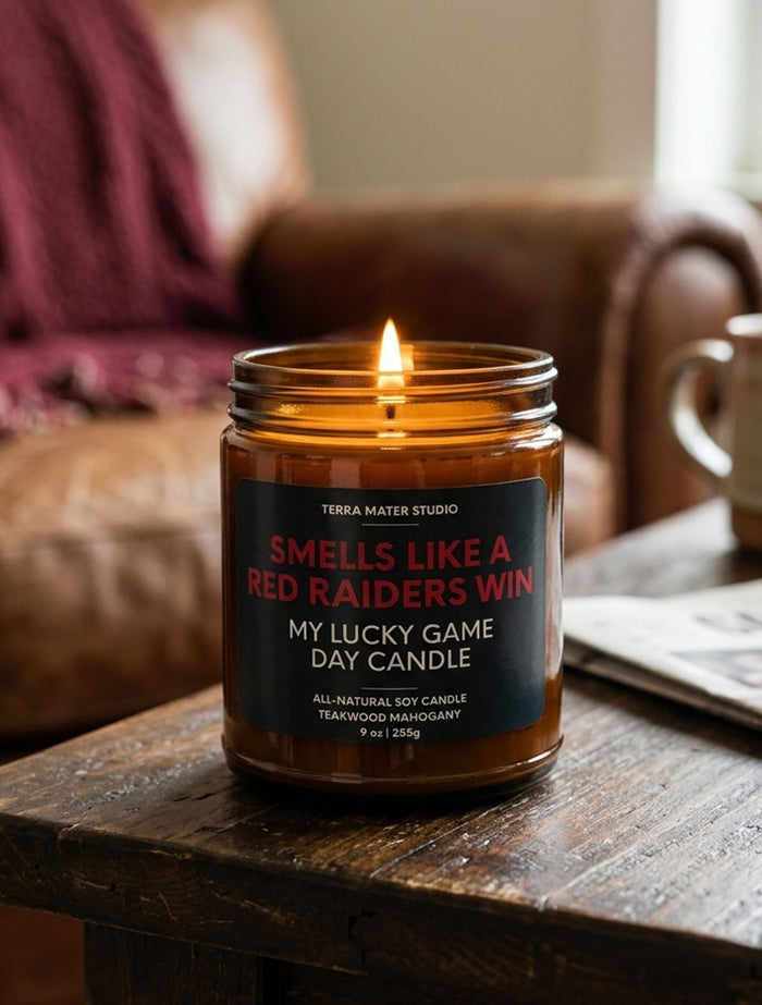 Smells Like A Red Raiders Win soy candle burning in an amber glass jar on a wooden table beside a leather chair
