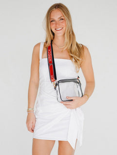 Model in a white wrap dress holding the clear crossbody purse at her hip, the red Wreck ’Em Tech strap running over her shoulder