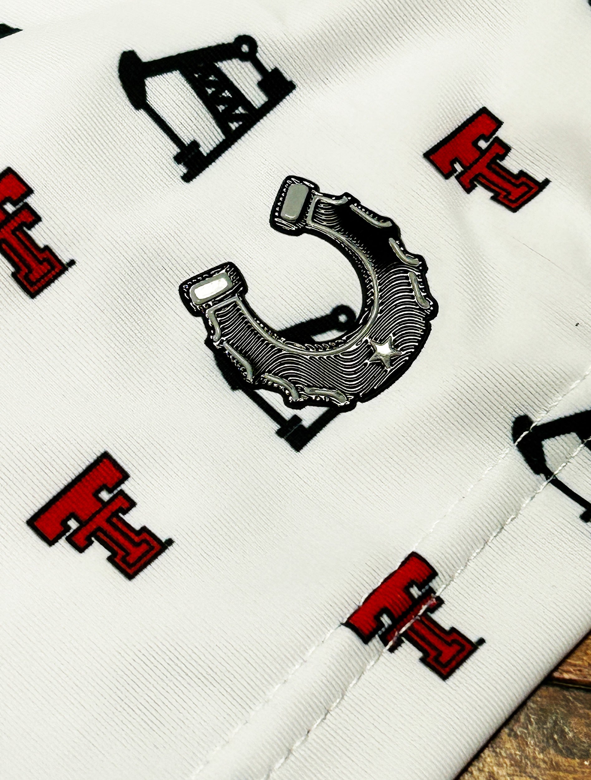 Close up of the chrome finish Dark Horse horseshoe patch on the sleeve of the white Texas Tech polo