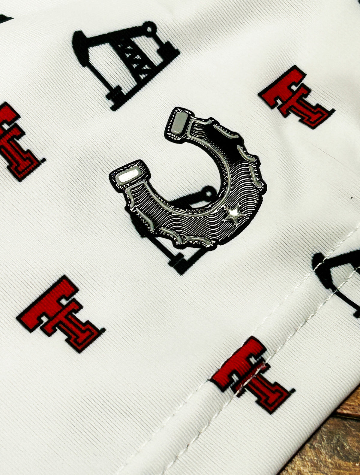 Close up of the chrome finish Dark Horse horseshoe patch on the sleeve of the white Texas Tech polo