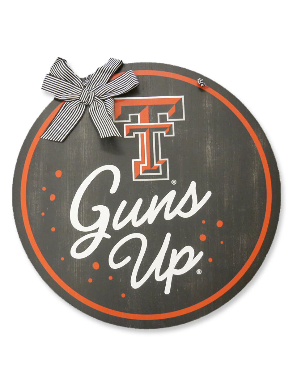 Black round wood door hanger with a red ring border, the Double T above Guns Up in white script, and a black and white striped ribbon bow